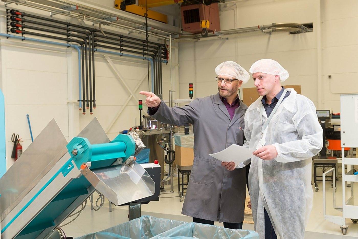 Twee medewerkers bij een productielijn in een bedrijfspand met een technische installatie van Hazeleger