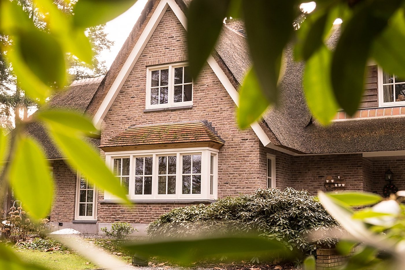 Bakstenen villa met rieten kap, gezien door het groen